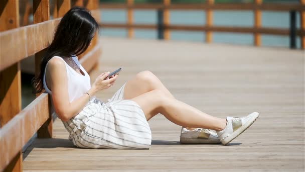 Femme mignonne lit le message texte sur le téléphone portable tout en étant assis dans le parc. — Video