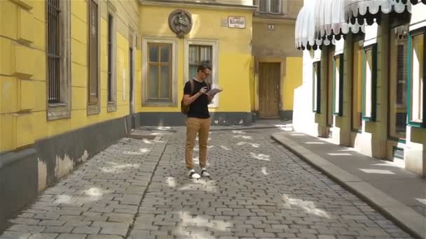 Homem turista com um mapa da cidade e mochila na Europa rua. Garoto caucasiano olha com mapa da cidade europeia . — Vídeo de Stock