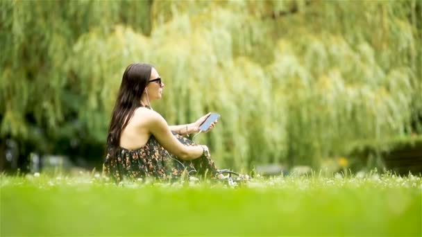 Aranyos nő olvas szöveges üzenetet a mobiltelefon, miközben ül a parkban. — Stock videók