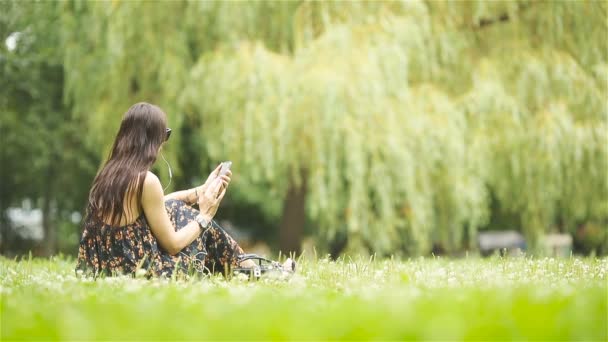 Schattige vrouw leest SMS-bericht op mobiele telefoon tijdens het zitten in het park. — Stockvideo