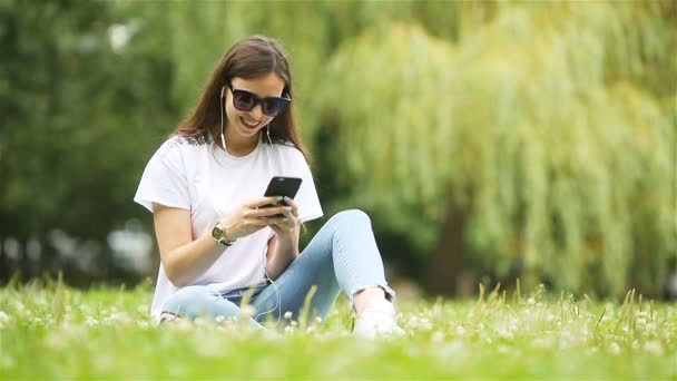 Cute woman is reading text message on mobile phone while sitting in the park. — Stock Video