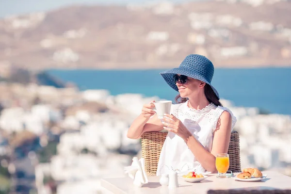 Jonge vrouw met koffie op het terras met prachtig uitzicht op Mykonos stad. — Stockfoto