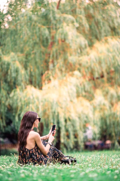 Söt kvinna läser textmeddelande på mobiltelefon när du sitter i parken. — Stockfoto