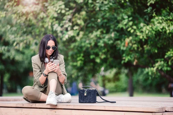 Femme mignonne lit le message texte sur le téléphone portable tout en étant assis dans le parc. — Photo