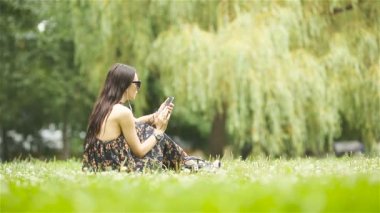 Şirin kadın parkta otururken cep telefonundan mesaj okuyor..