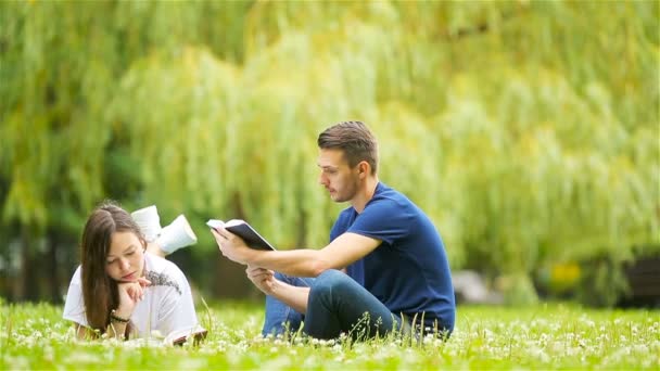 Relajada pareja joven leyendo libros mientras está acostado en la hierba — Vídeo de stock