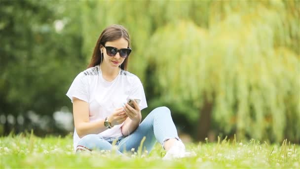 Cute woman is reading text message on mobile phone while sitting in the park. — Stock Video