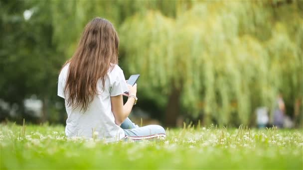 귀여운 여자 가 공원에 앉아 있는 동안 휴대 전화로 문자 메시지를 읽고 있다. — 비디오