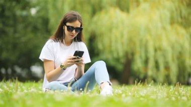 Şirin kadın parkta otururken cep telefonundan mesaj okuyor..
