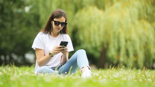 Schattige vrouw leest SMS-bericht op mobiele telefoon tijdens het zitten in het park. — Stockvideo