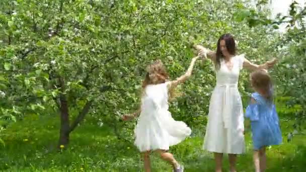 Meninas adoráveis com a jovem mãe no jardim florido no belo dia de primavera se divertindo juntos — Vídeo de Stock