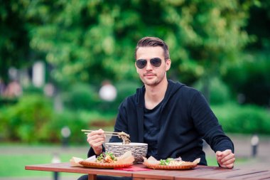 Genç adam yeme Asya sokak gıda ile sopa ve fo portresi bo çorba açık Cafe