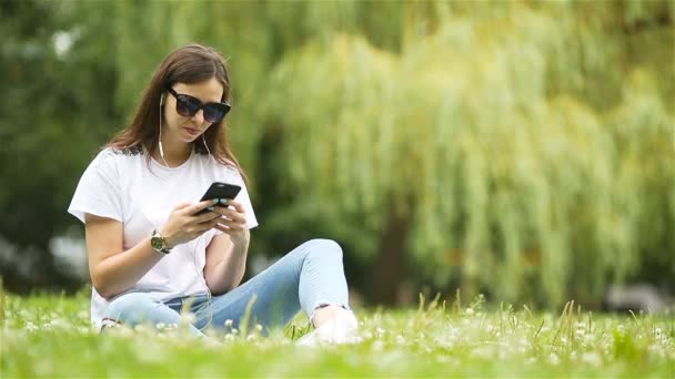 Roztomilá žena čte textovou zprávu na mobilním telefonu, zatímco sedí v parku. — Stock video