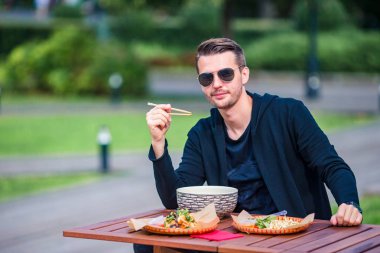Young man eating take away noodles on the street clipart