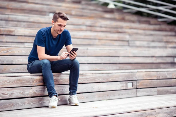 Человек читает текстовые сообщения на мобильном телефоне во время прогулки по парку — стоковое фото
