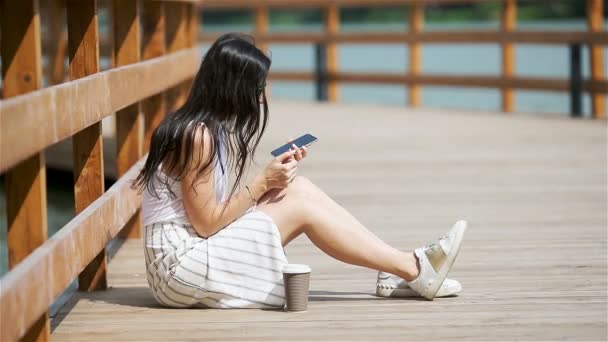 Χαριτωμένη γυναίκα διαβάζει το μήνυμα κειμένου στο κινητό τηλέφωνο, ενώ κάθεται στο πάρκο. — Αρχείο Βίντεο
