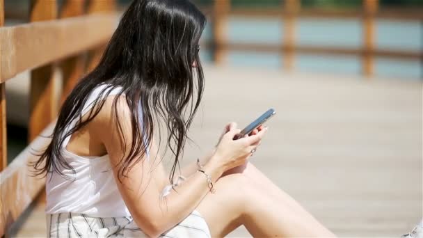 公園に座っている間、かわいい女性は携帯電話でテキストメッセージを読んでいます. — ストック動画