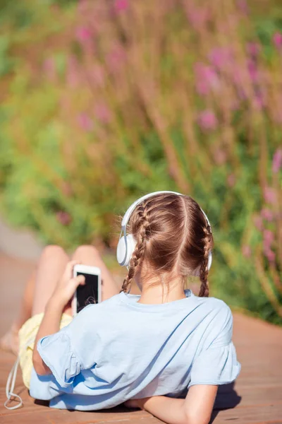 Malá rozkošná dívka poslouchá hudbu v parku — Stock fotografie