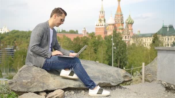 El hombre está trabajando por ordenador portátil mientras se relaja en el parque — Vídeo de stock