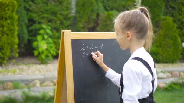 Happy little schoolgirl with a chalkboard outdoor — Stock Video