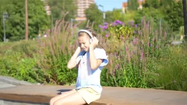 Klein schattig meisje luisteren muziek in het park — Stockvideo