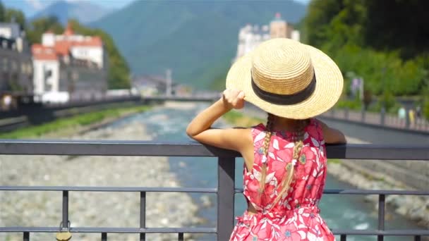 Little girl at hat on the embankment of a mountain river in a European city. — Stock Video