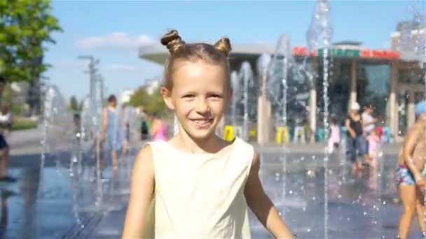 Маленькая очаровательная девушка весело провести время в уличном фонтане в жаркий солнечный день — стоковое видео