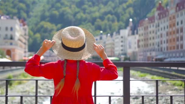 Kleines Mädchen mit Hut am Ufer eines Gebirgsflusses in einer europäischen Stadt. — Stockvideo