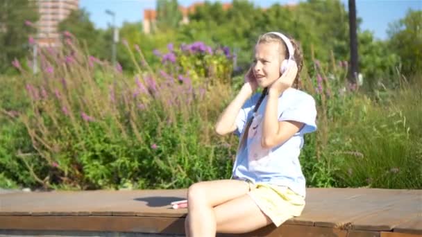 Маленькая очаровательная девочка слушает музыку в парке — стоковое видео