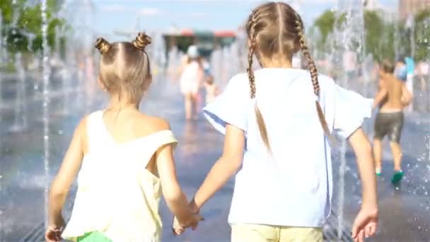 Pequeñas chicas adorables se divierten en la fuente de la calle en el día soleado caliente — Vídeo de stock