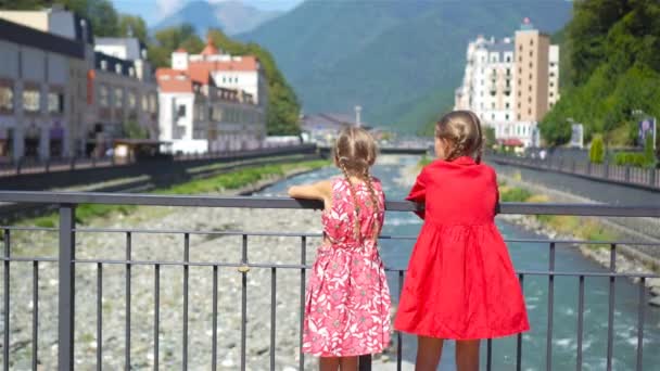 Kleine meisjes bij hat aan de kade van een rivier berg in een Europese stad. — Stockvideo