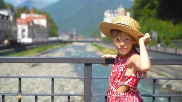 Niña de sombrero en el terraplén de un río de montaña en una ciudad europea . — Vídeos de Stock