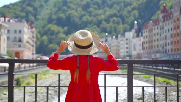 Niña de sombrero en el terraplén de un río de montaña en una ciudad europea . — Vídeos de Stock