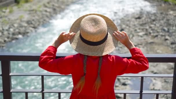 Little girl at hat on the embankment of a mountain river in a European city. — Stock Video