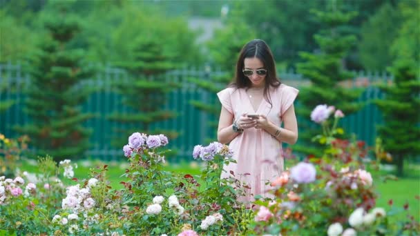Chica joven en un jardín de flores entre hermosas rosas. Huele a rosas. — Vídeo de stock