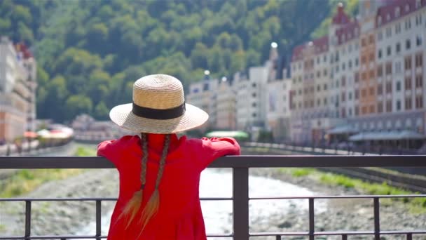 Niña de sombrero en el terraplén de un río de montaña en una ciudad europea . — Vídeos de Stock