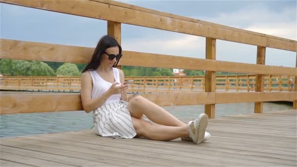 Femme mignonne lit le message texte sur le téléphone portable tout en étant assis dans le parc. — Video