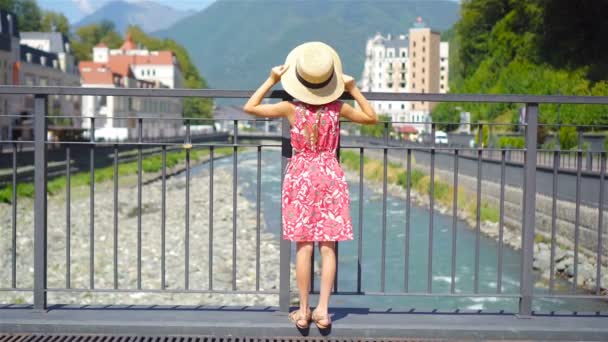 Niña de sombrero en el terraplén de un río de montaña en una ciudad europea . — Vídeos de Stock