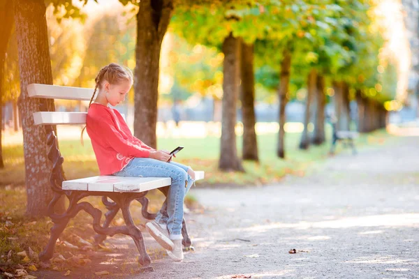 Liten bedårande flicka med smartphone i höst. — Stockfoto