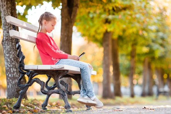 Niña adorable con teléfono inteligente en otoño . — Foto de Stock