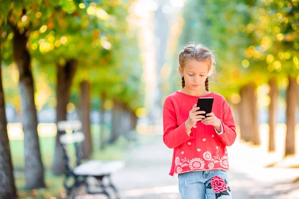 Kleines entzückendes Mädchen mit Smartphone im Herbst. — Stockfoto