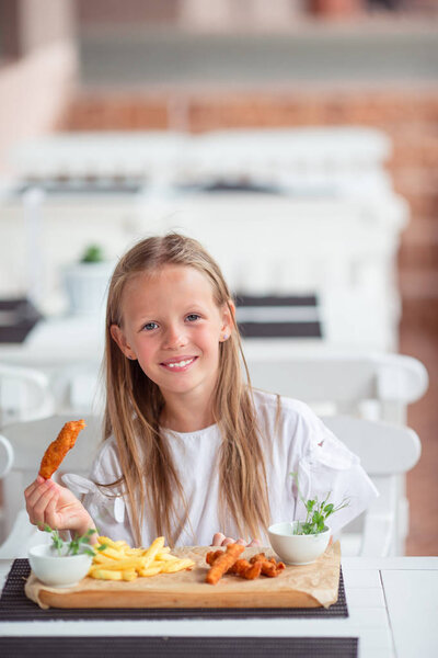 Очаровательная девочка обедает в кафе на открытом воздухе
