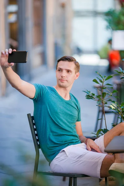 Turista caucásico con smartphone tomando selfie sentado en la cafetería al aire libre . — Foto de Stock