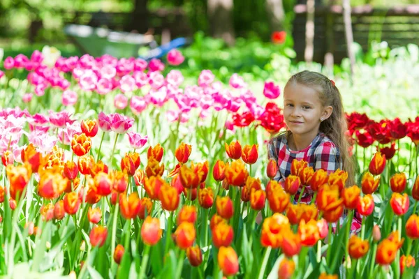 Kleines entzückendes Mädchen, das bunte Tulpen im Sommergarten riecht — Stockfoto