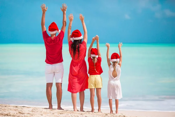 Happy family in red Santa hats on a tropical beach celebrating Christmas vacation — Stock Photo, Image