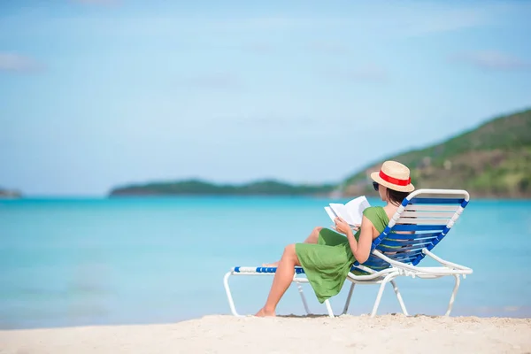 Joven mujer leyendo libro sobre chaise-lounge en la playa —  Fotos de Stock