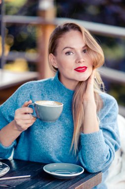 Sonbahar konsepti: Sonbahar parkında sonbahar yaprakları altında kahve içen güzel bir kadın.