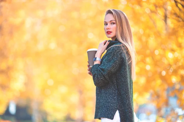 Podzimní koncepce - krásná žena pije kávu v podzimním parku pod podzimní listí — Stock fotografie