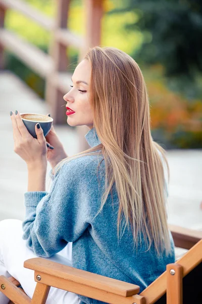 El concepto de otoño - la mujer hermosa que bebe café en el parque otoñal bajo el follaje otoñal —  Fotos de Stock