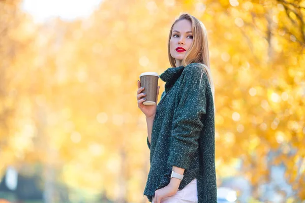 Fall concept - beautiful woman drinking coffee in autumn park under fall foliage — Stock Photo, Image